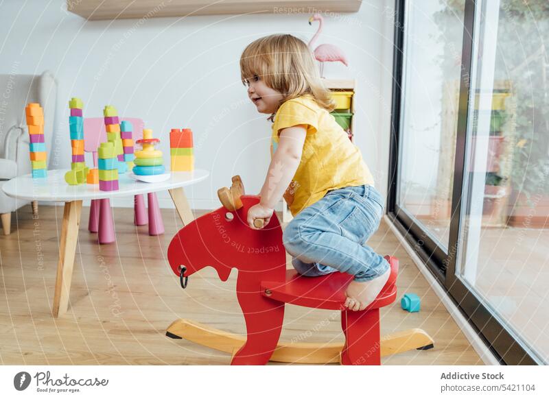 Glückliches Kind reitet Spielzeugpferd im Kinderzimmer spielen Pferd Mitfahrgelegenheit Spaß Freude farbenfroh Säugling wenig Baby Bildung Kindheit bezaubernd