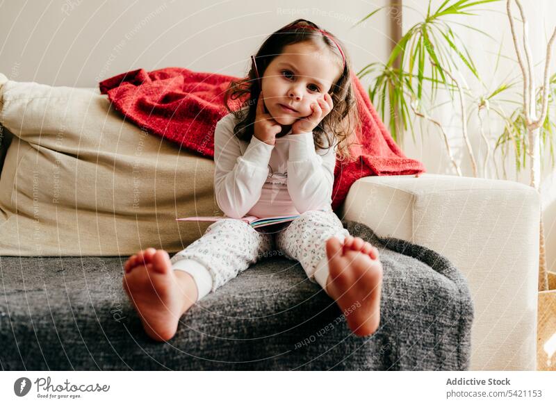 Niedliches kleines Mädchen sitzt auf der Couch und sucht nach Inspiration niedlich wenig posierend heimwärts im Innenbereich Fenster Kind Porträt Kindheit