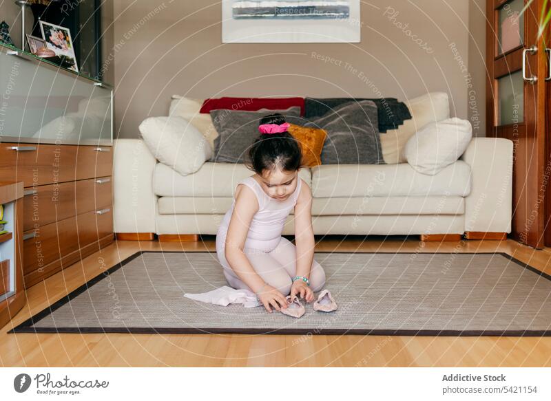 Kleine Ballerina beim Anziehen der Tanzschuhe kleines Mädchen Balletttänzer angezogen Schuh heimwärts Probe vorbereiten sitzen Stock Wohnzimmer Sofa Teppich
