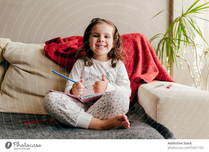 Niedliches kleines Mädchen sitzt auf der Couch und zeichnet in ein Notizbuch niedlich wenig posierend heimwärts im Innenbereich Fenster Kind Porträt Kindheit
