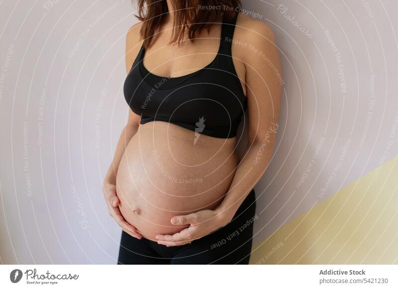 Crop schwangere Frau in der Nähe der Wand im Yoga-Studio Atelier Pause berühren Bauch fettarm Training Sportbekleidung Gesundheit Wellness Wohlgefühl erwarten
