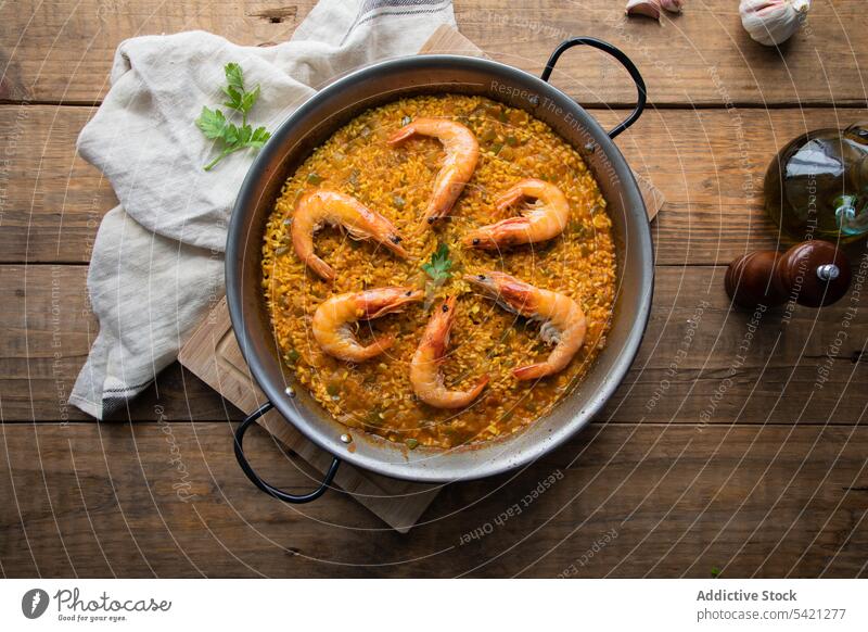 Große Pfanne mit herzhaftem Reisgericht und aromatischen, lecker gebratenen Garnelen auf einem Holztisch Paella Granele Handtuch Lebensmittel rustikal