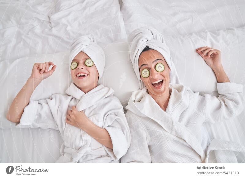 Fröhliche Frau mit Kind genießt Wellnessbehandlung zu Hause Schönheit Hautpflege Salatgurke Mundschutz Mutter Zusammensein Spaß haben genießen Lachen ruhen