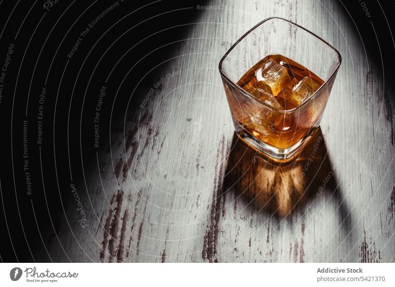 Glas Scotch in Strahlen auf alten rustikalen Tisch in der Dunkelheit Whiskey Bourbon Alkohol Getränk Eis trinken liquide Schnaps Cognac Weinbrand durchsichtig