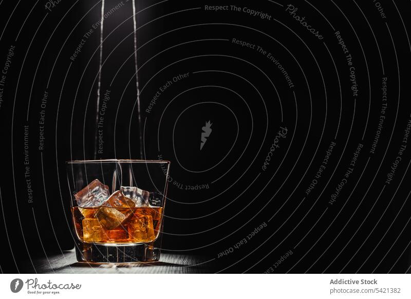Glas Whiskey mit Eiswürfeln in Lichtstrahlen auf Tisch in dunklem Raum Scotch Bourbon Alkohol Getränk trinken liquide Schnaps Cognac Weinbrand durchsichtig
