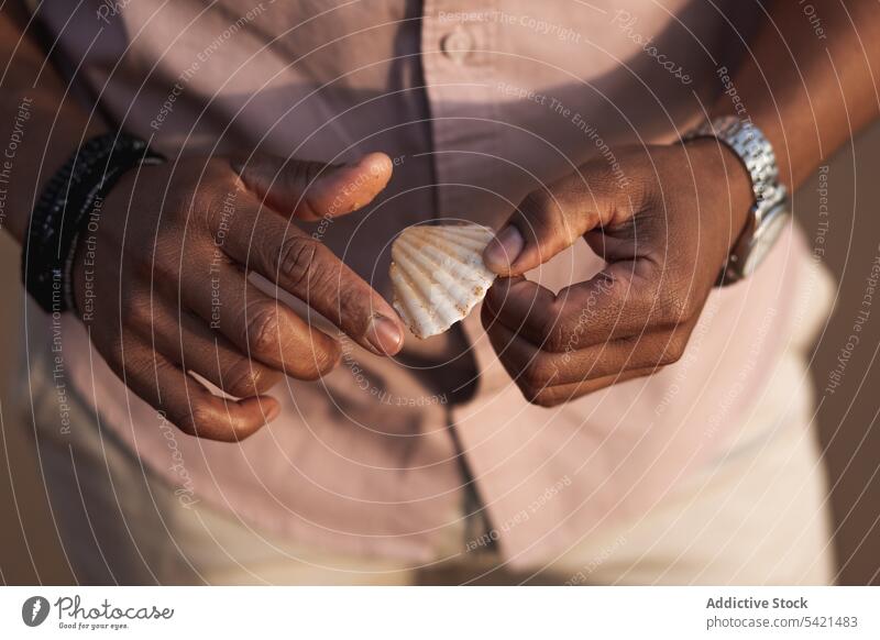 Ethnischer Mann mit Accessoires hält Muschel Armband Armbanduhr Hand Stil Mode trendy Sommer männlich Design maskulin schwarz ethnisch Typ Detailaufnahme