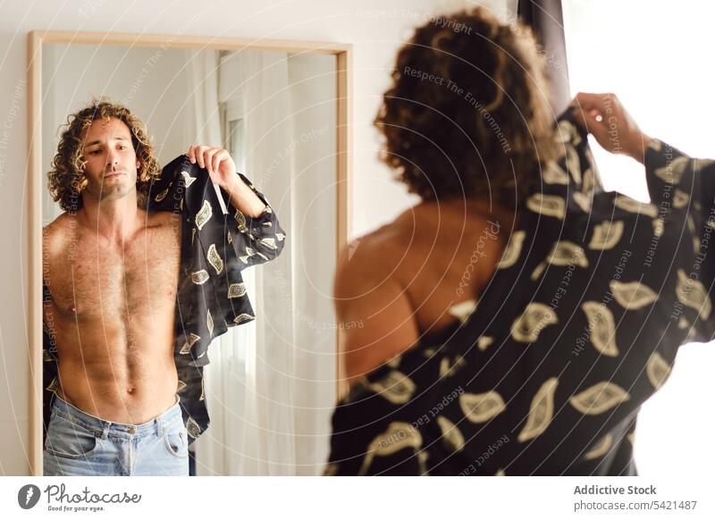 Ein fitter Mann zieht ein Hemd an und schaut in den Spiegel angezogen passen verkleiden heimwärts Stoff Outfit Stil männlich Raum Reflexion & Spiegelung modern