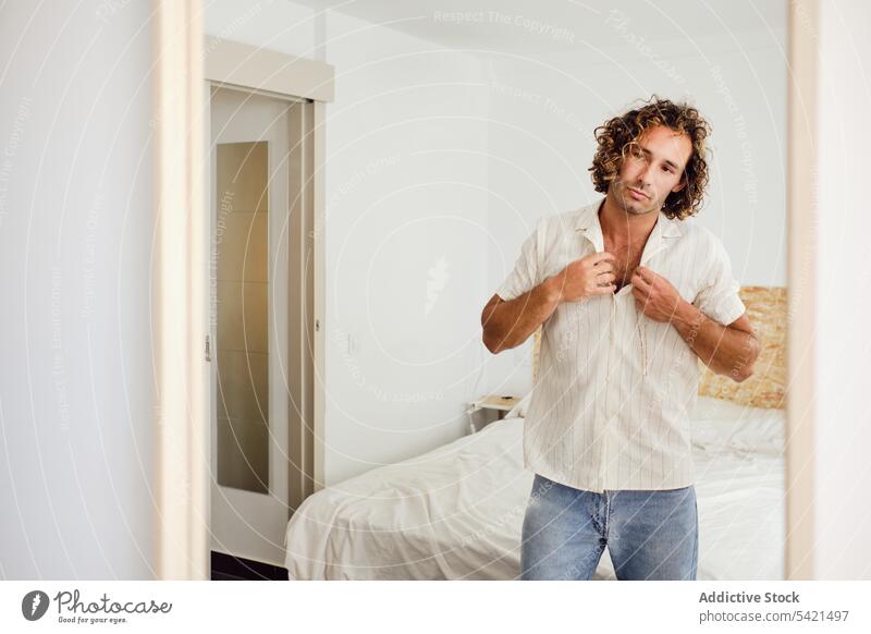 Hübscher Mann knöpft Hemd im Zimmer zu Schaltfläche angezogen verkleiden Reflexion & Spiegelung Stil gutaussehend Outfit männlich heimwärts Raum modern