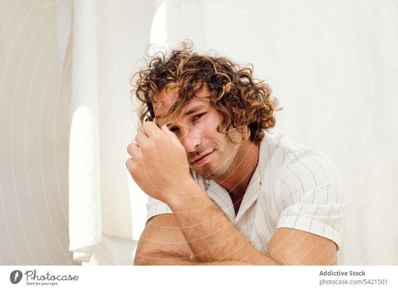 Lächelnder Mann mit lockigem Haar schaut in die Kamera auf weißem Hintergrund gutaussehend krause Haare Vorschein Freude Stuhl Teint Stil