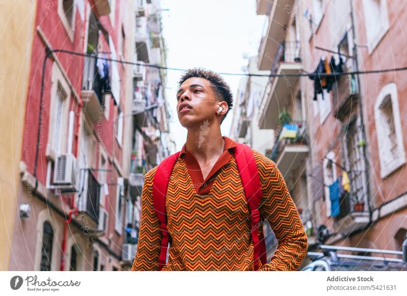 Stilvoller ethnischer Mann auf der Straße in der Stadt Reisender urban Ohrstöpsel selbstbewusst zuhören trendy erkunden männlich jung hispanisch Tourist Urlaub