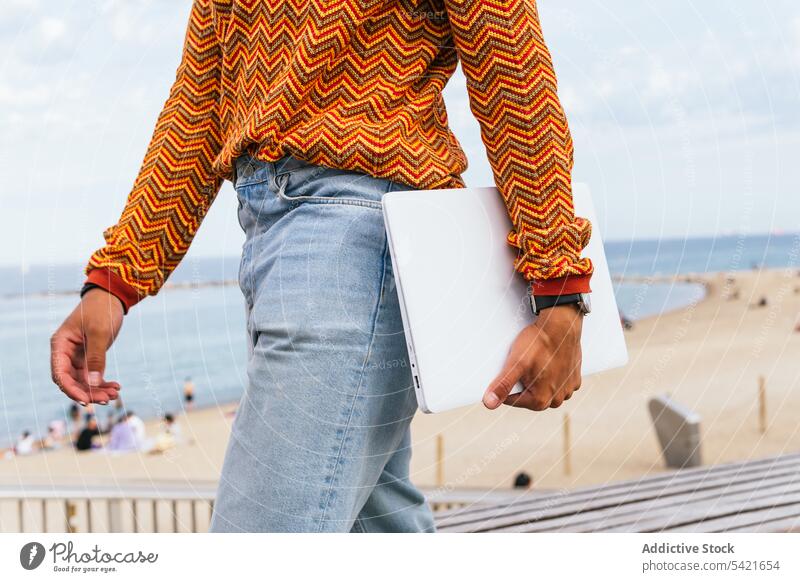 Stilvoller Mann mit Laptop bei einem Spaziergang am Meer trendy Strand modern Apparatur digital farbenfroh urban ethnisch männlich Streifen Sommer MEER