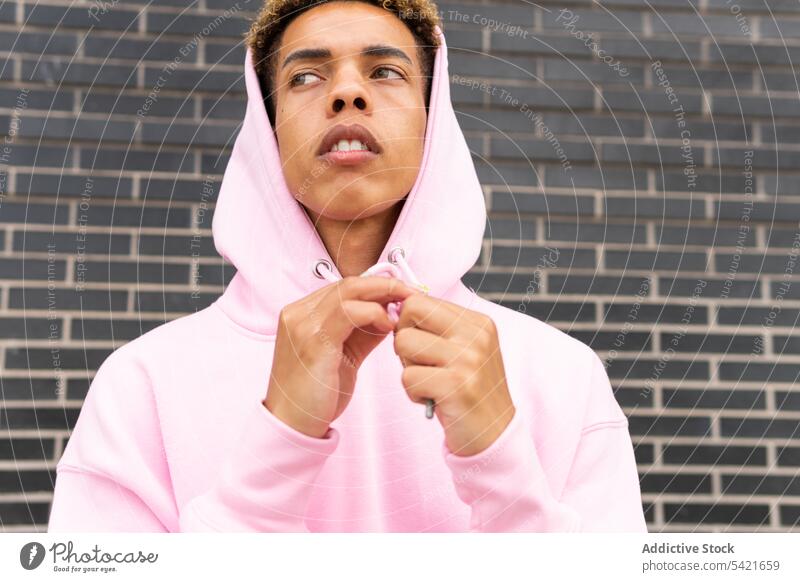 Junger ethnischer Mann in rosa Kapuzenpulli Stil selbstbewusst Hipster urban Mode Outfit ernst jung trendy modern männlich krause Haare Afro-Look Individualität