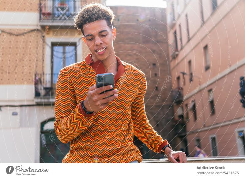 Ethnischer Mann benutzt Smartphone in der Stadt benutzend urban Stil Telefon Browsen modern Sonnenlicht Mobile männlich jung hispanisch Lateinamerikaner