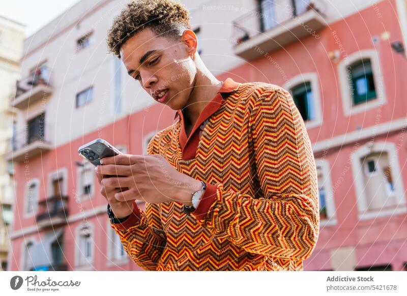 Ethnischer Mann benutzt Smartphone in der Stadt benutzend urban Stil Telefon Browsen modern Sonnenlicht Mobile männlich jung hispanisch Lateinamerikaner