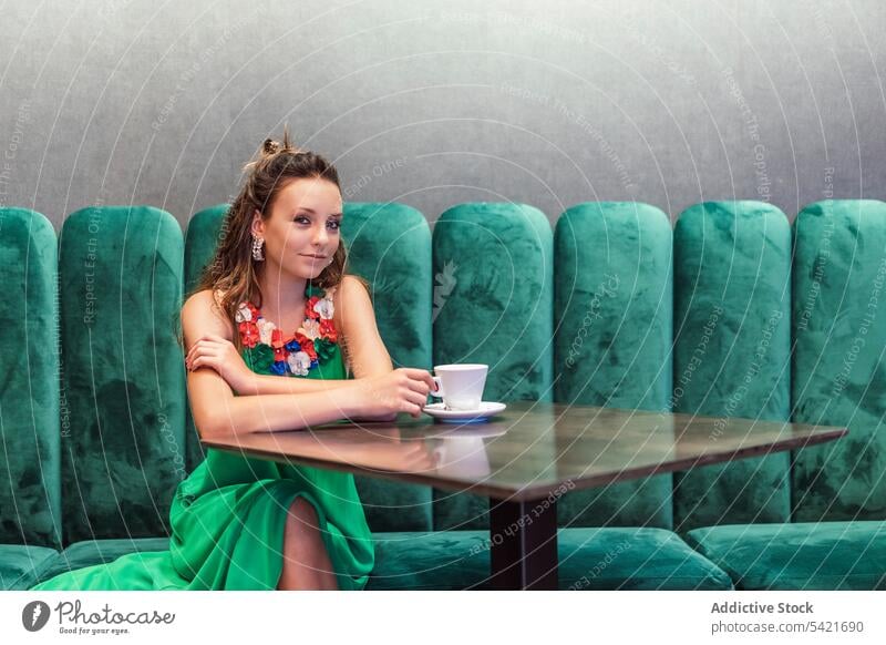 Junge Frau in modischem grünem Kleid ruht sich in einem Café aus Mode Stil Farbe elegant Kaffee hell Model jung Teenager geblümt Ohrringe charmant farbenfroh