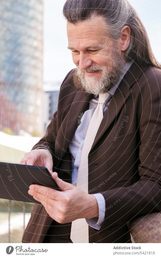 Älterer bärtiger Geschäftsmann benutzt Tablette auf der Straße benutzend Apparatur digital Vollbart urban formal Kommunizieren online Mann Browsen Gerät positiv