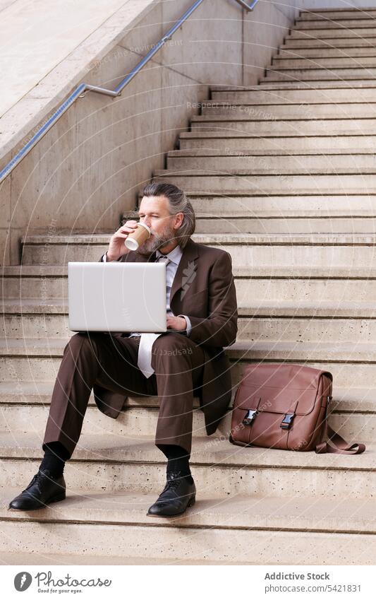 Älterer Mann im Anzug benutzt Laptop auf einer Treppe Geschäftsmann benutzend online abgelegen Stil Glück Apparatur Internet Kommunizieren Unternehmer positiv