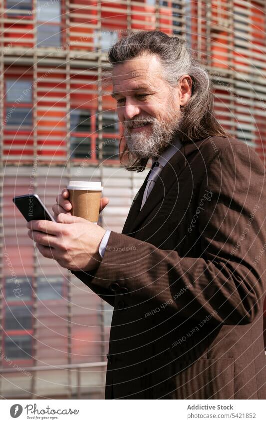 Älterer Geschäftsmann mit Kaffee und Smartphone benutzend Apparatur Telefon Imbissbude Tasse Lächeln Vollbart modern Mann reif Lebensmitte Exekutive graues Haar