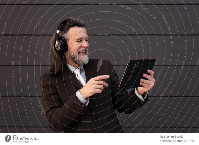 Glücklicher reifer Geschäftsmann mit Kopfhörer und Tablet Tablette digital online Kommunizieren zuhören Apparatur benutzend Stil Mann Lebensmitte graues Haar