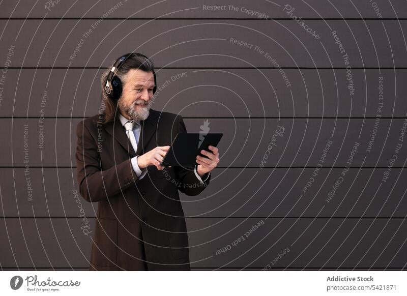 Glücklicher reifer Geschäftsmann mit Kopfhörer und Tablet Tablette digital online Kommunizieren zuhören Apparatur benutzend Stil Mann Lebensmitte graues Haar