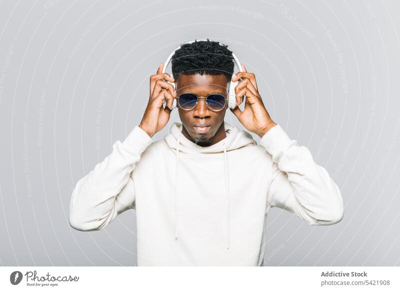 Fröhlicher schwarzer Mann in trendigem Outfit hört Musik Kopfhörer Stil zuhören Hipster weiß trendy Sonnenbrille Kapuzenpulli Mode jung Afroamerikaner ethnisch