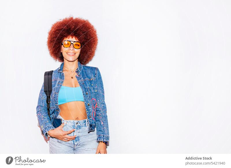 Fröhliche Frau mit Afrofrisur Afro-Look Stil Mode trendy Bekleidung Wand Vorschein Outfit Rucksack Straße Frisur Sonnenbrille Accessoire Top attraktiv