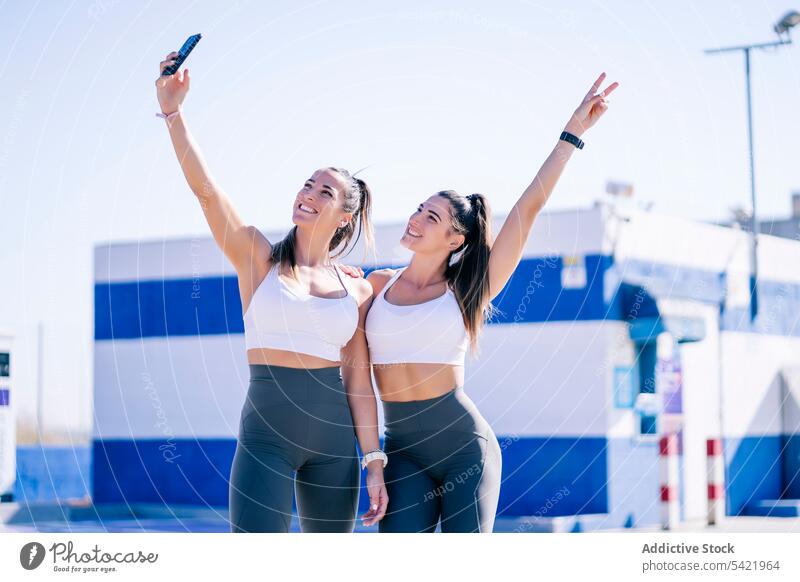 Fröhliche Zwillingsschwestern machen ein Selfie auf dem Sportplatz Frauen heiter Smartphone passen Schwester benutzend sportlich Zusammensein Selbstportrait