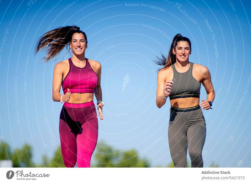Fröhliche sportliche Zwillinge beim gemeinsamen Laufen joggen laufen passen Fitness Training Frauen Pferdeschwanz Schwester Zusammensein heiter positiv