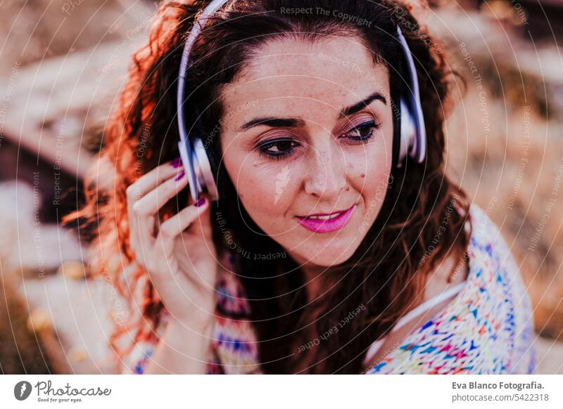 Porträt im Freien von einer jungen schönen Frau bei Sonnenuntergang Musik hören auf Kopfhörer und lächelnd. Lifestyle und Musik Konzept lässig Spaß