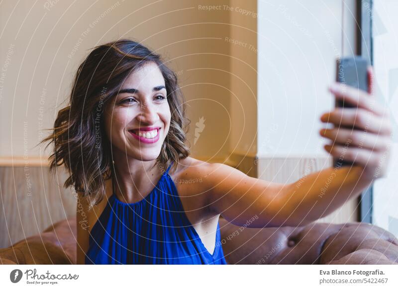 Junge schöne Frau, die ein Selfie mit Handy macht und lächelt. Sie trägt ein lässiges blaues Kleid. Innenräume, Technologie und Lebensstil Porträt Mobile Person