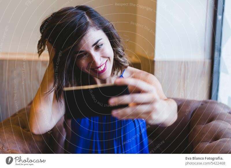 Junge schöne Frau, die ein Selfie mit Handy macht und lächelt. Sie trägt ein lässiges blaues Kleid. Innenräume, Technologie und Lebensstil Porträt Mobile Person