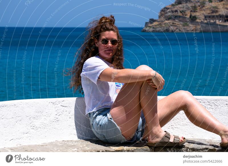 Junge Lady  mit Sonnenbrille lehnt sich lässig an eine kleine Mauer. Hinter ihr das blaue Meer von Kreta. Dame Außenaufnahme feminin Farbfoto Erwachsene