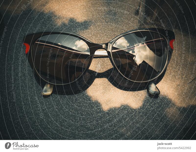 Brille mit dunkel getönten Gläsern, die auf einer Tischplatte liegt und den Himmel reflektiert Sonnenbrille Frau Reflexion & Spiegelung stylisch Wolken Sommer