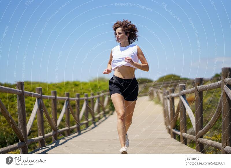 Sportlerin, die an einem sonnigen Tag einen Holzweg entlang läuft joggen Fitness Aufwärmen Übung Training Athlet Promenade laufen Frau Jogger Wohlbefinden