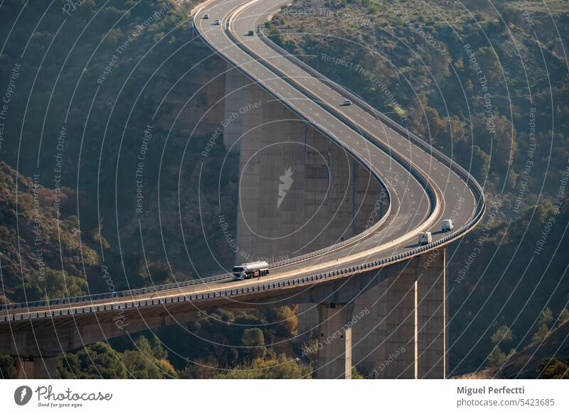 Riesiges Viadukt, das eine Schlucht überquert, mit einem Tankwagen und mehreren Fahrzeugen, die auf der Straße verkehren, Ansicht von oben. Autobahn Kurve