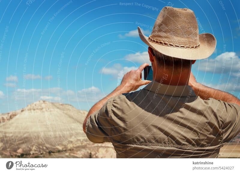 Mann mit Hemd und Cowboyhut, der beim Trekking in den Bergen Fotos mit dem Mobiltelefon macht unter Telefon wandern Natur im Freien laufen Hut acivity