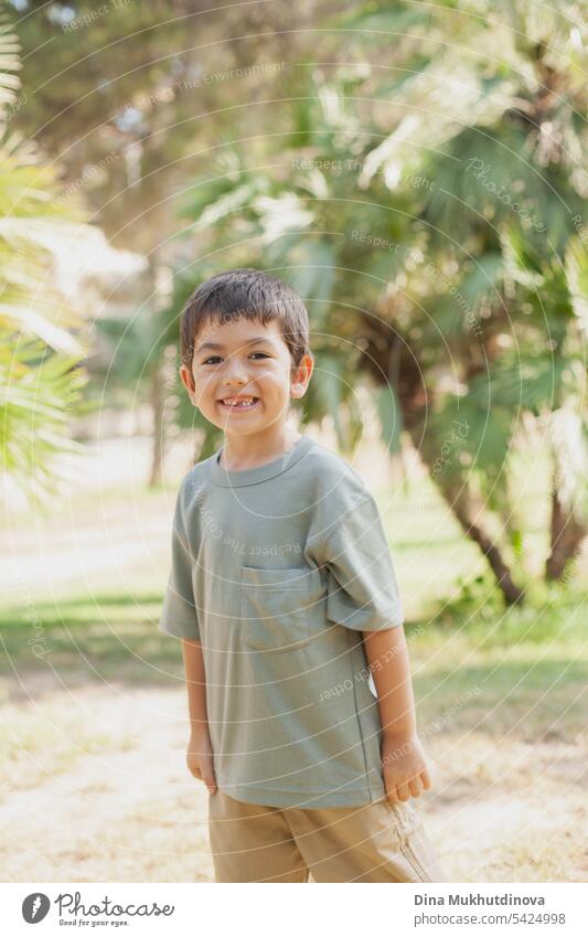 diverses Kind im Park stehend, lächelnd und in die Kamera schauend. Fünf oder sechs Jahre alter Junge im Park im Sommer mit Palmen als Hintergrund. 5 Jahre alt