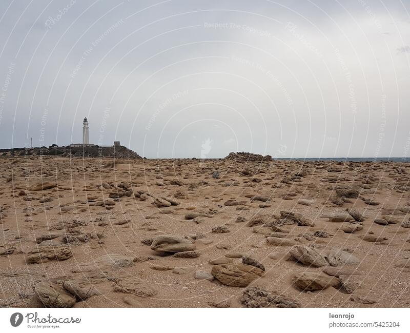 Eine verträumte und romantische Szene auf eine Steinwüste am Meer. Im Hintergrund sieht man den Leuchturm von Trafalgar an der Costa de la Luz in Andalusien.