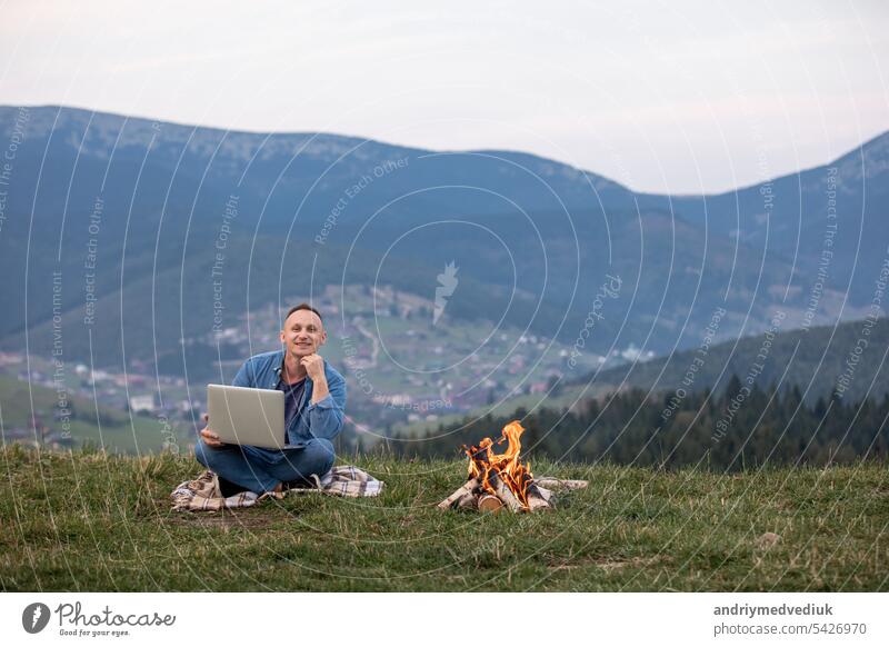 Mann arbeitet im Freien mit Laptop in den Bergen sitzend. Konzept der Remote-Arbeit oder Freiberufler Lebensstil. Zelluläre Netzwerk-Breitband-Abdeckung. Internet 5G. Wanderer Tourist genießt Talblick