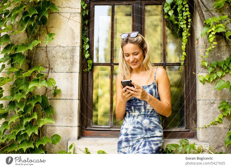 Hübsche junge Frau, die ein Handy benutzt, neben einem alten Haus mit Efeu Glück schön Funktelefon hübsch Mobile Menschen Lifestyle Telefon Smartphone klug