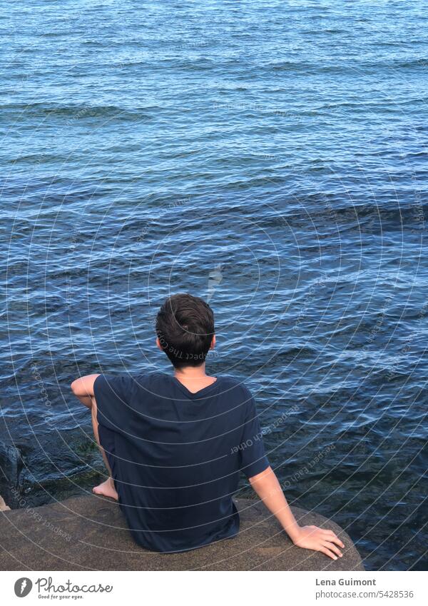 Junge sitzt auf Felsen und schaut auf Meer Wellen Hand Wasser Natur Außenaufnahme Sommer Ferien & Urlaub & Reisen Farbfoto Erholung Tag blau Schönes Wetter