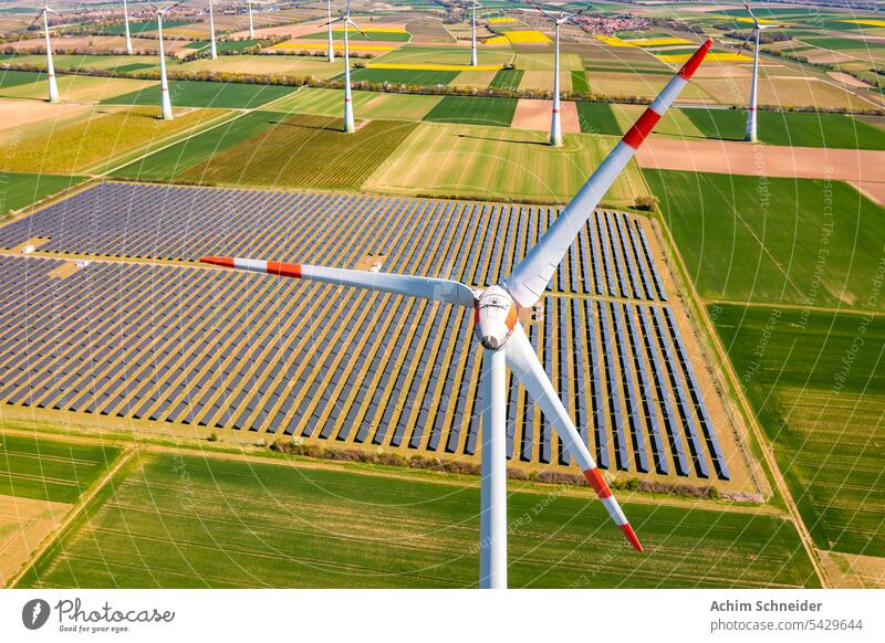 Luftaufnahme einer Windkraftanlage vor landwirtschaftlichen Feldern und PV-Paneelen eines Solarparks Windturbinen landwirtschaftliche Flächen agri-PV riesig