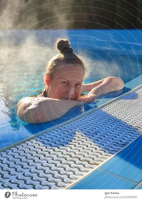 Nahaufnahme einer lächelnden jungen Frau, die sich in der Morgensonne an den Rand eines beheizten Swimmingpools lehnt Schwimmen & Baden Lächeln Schwimmbad