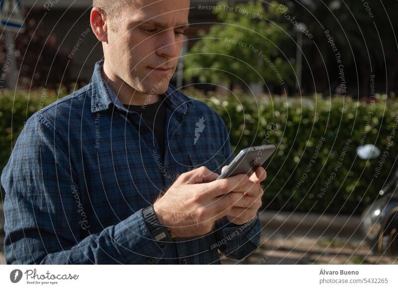 Ein kaukasischer Mann mittleren Alters schaut auf der Straße an einem sonnigen Tag auf sein Smartphone, um Informationen abzurufen. Männer Person