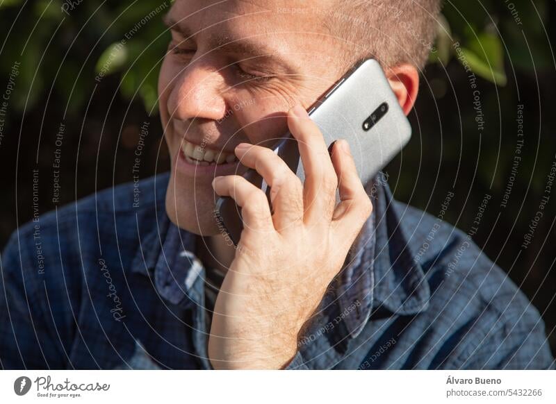 Ein Mann, der sich an einem sonnigen Tag auf der Straße angeregt und lächelnd mit einem Handy unterhält männlich Telefon Mobile Person Erwachsener Kaukasier