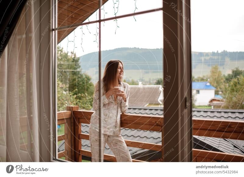 Junge Frau stehend nach dem Duschen am Morgen auf dem Balkon des Hotels. hält eine Tasse Kaffee oder Tee in ihren Händen. Blick nach draußen Natur Wald und Berg