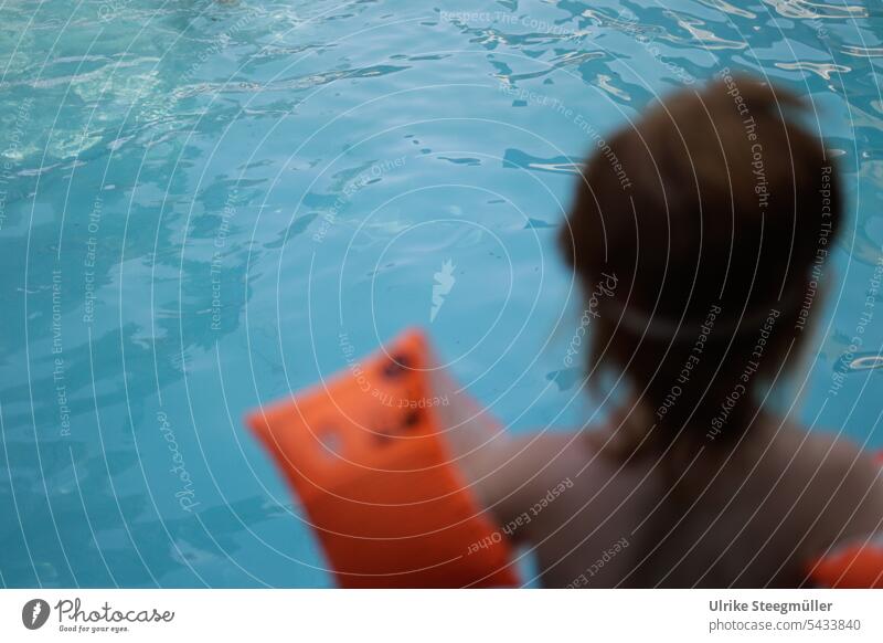 Ein Kind steht am Schwimmbeckenrand Urlaub mit Kindern Sommerurlaub Leben mit Kindern Schwimmflügel orange blau Schwimmen lernen tauchen schwimmen Hitze