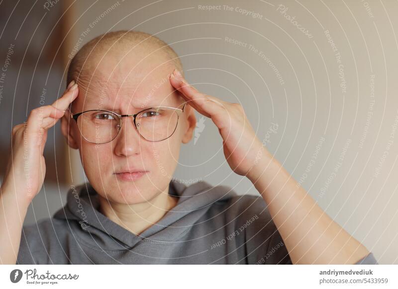 Haarlose Frau mit Brille, die mit den Händen den Kopf berührt, leidet unter Kopfschmerzen nach einer Chemotherapie. Unglückliche kahle krebskranke Patientin mit Migräne zu Hause. Onkologie-Konzept. Gesundheitswesen, Medizin