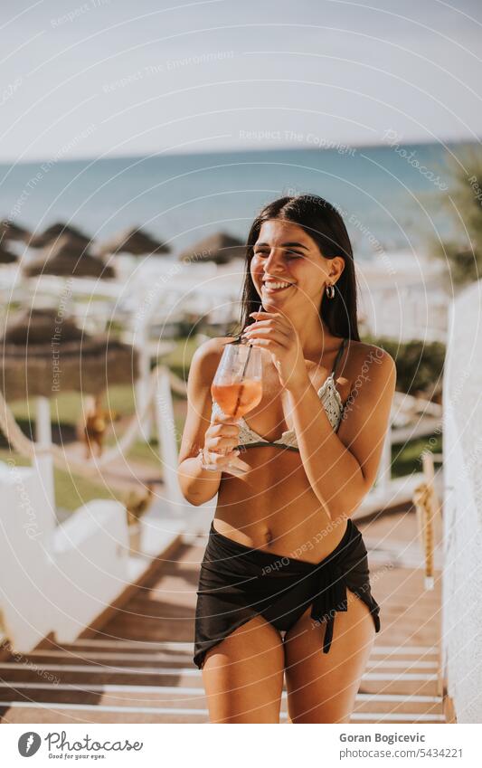 Lächelnde junge Frau im Bikini, die ihren Urlaub am Strand genießt trinken Italien Stroh Seeküste Erwachsener Bekleidung Fröhlichkeit Feiertag