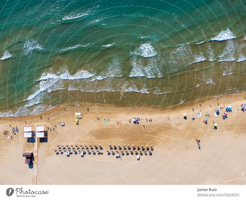 zenithale Luftaufnahme eines Strandes im Sommer mit Badegästen, Wasserskates und reetgedeckten Sonnenschirmen zum Verleih, behindertengerechter Rampe und Aussichtsturm von oben gesehen, Drohnenansicht